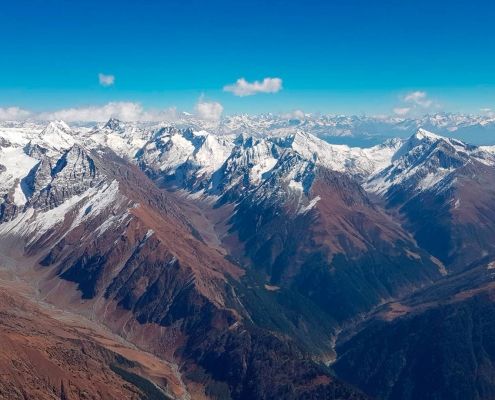 Flugaufnahme: Hohe Berge, hohe Wolkenbasis und im Hintergrund noch viel höhere Berge in kristallklarer Luft.