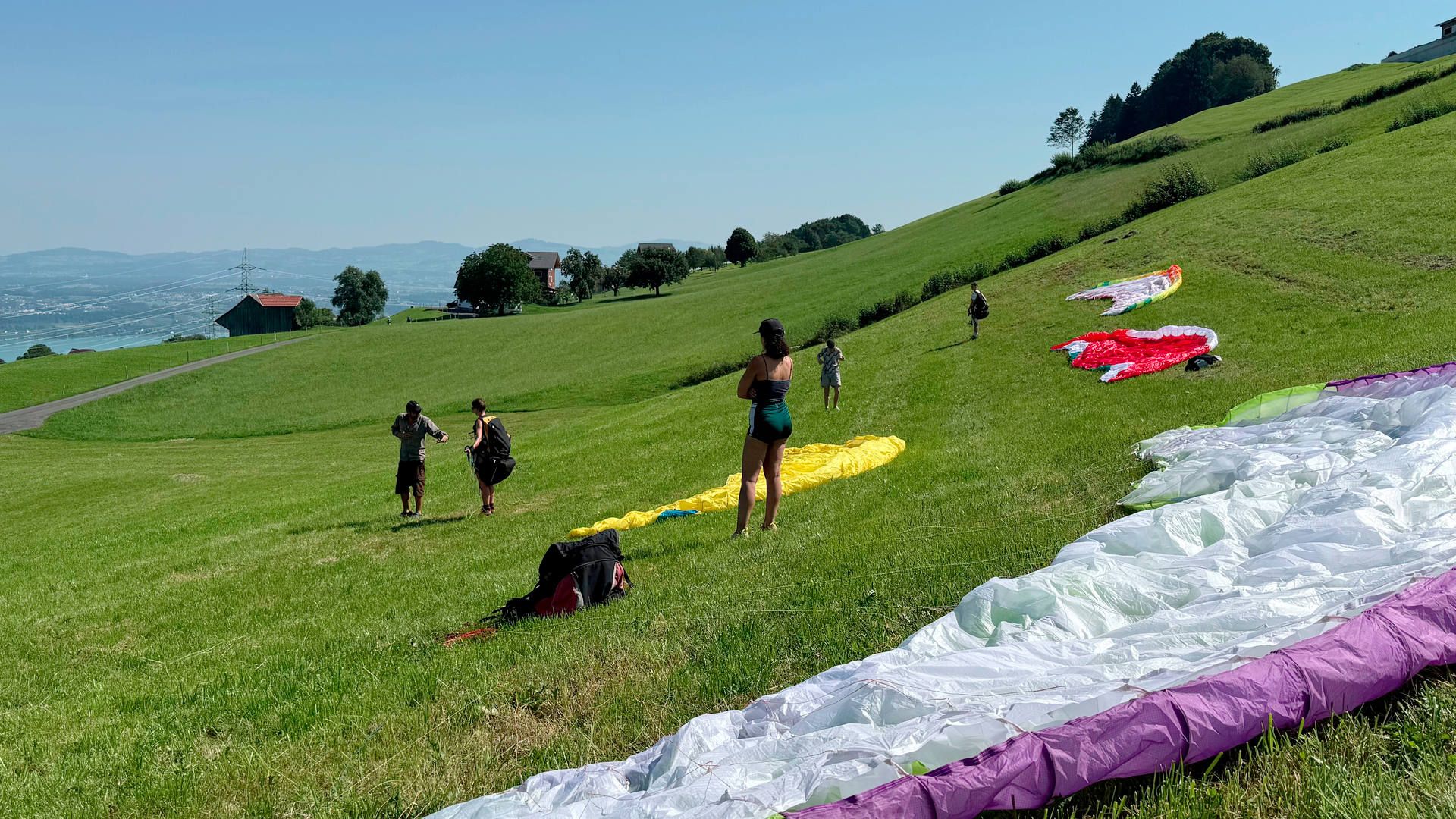 Teilnehmer beim Gleitschirm-Grundkurs haben die Schirme für eine Übung ausgelegt und bekommen letzte Anweisungen des Fluglehrers zum Vorflugcheck.