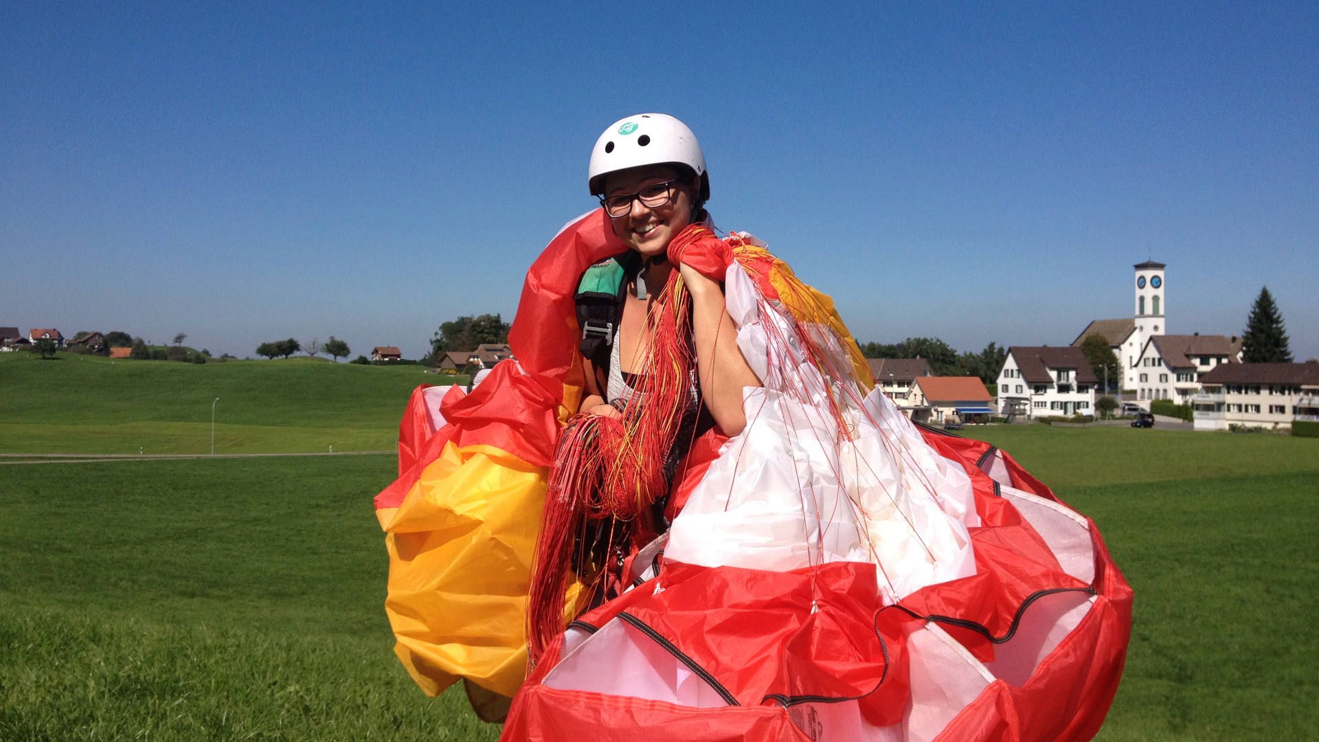 Eine glückliche Kursteilnehmerin rafft nach einem Gleitflug am Übungshang nach der Landung ihren Gleitschirm zusammen.
