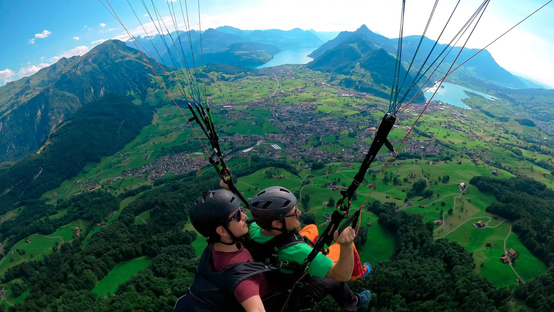 gleitschirm-tandemflug-sommer-passagier-steuert-schwyzer-talkessel-quer Flugaufnahme: Bei einem Tandemflug von der Rotenflueh übergibt der Pilot die Bremsleinen dem Passagier. Im Hintergrund der Schwyzer Talkessel, der Lauerzersee und ein Teil vom Vierwaldstättersee.