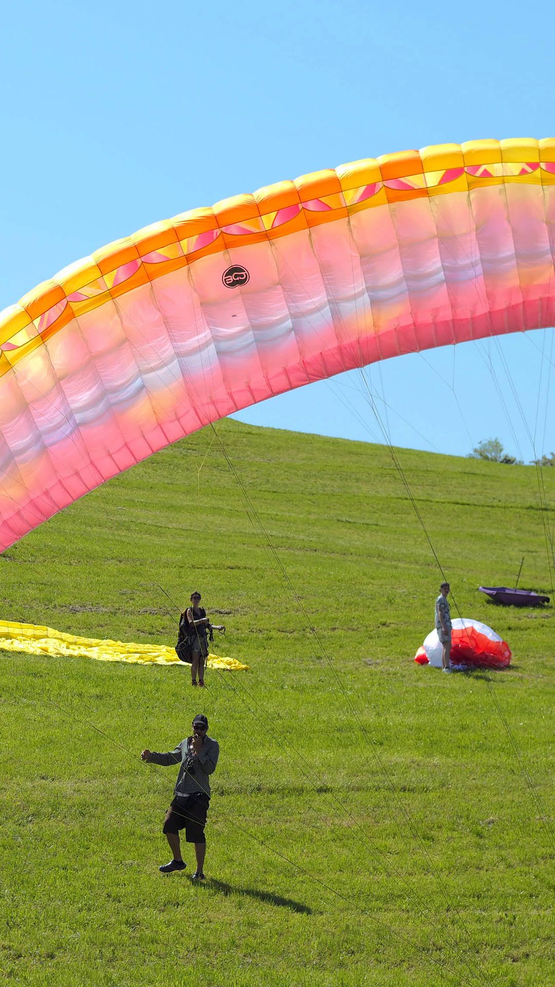 Aufgezogener Gleitschirm am Übungshang, im Hintergrund andere Kursteilnehmer bei ihren Startvorbereitungen.