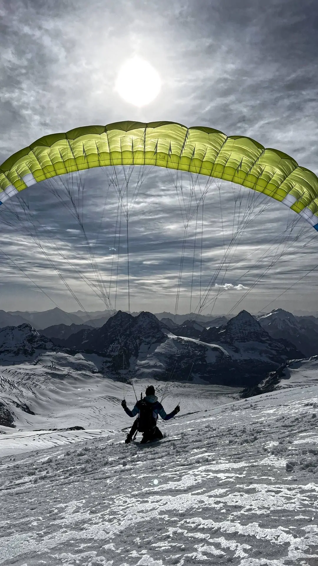 gleitschirmfliegen-groundhandling-hochalpin-winter-hoch Ein Pilot ist mit seinem Gleitschirm in hochalpinem Gelände eingelandet und spielt mit aufgezogenem Schirm im Wind auf dem Schnee.