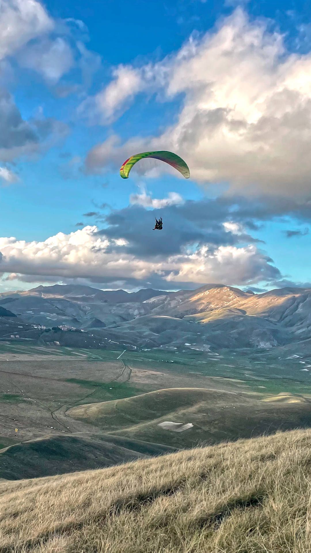 Ein Tandemschirm fliegt über der Ebene von Castelluccio im dynamischen Aufwind an einem Hügel.