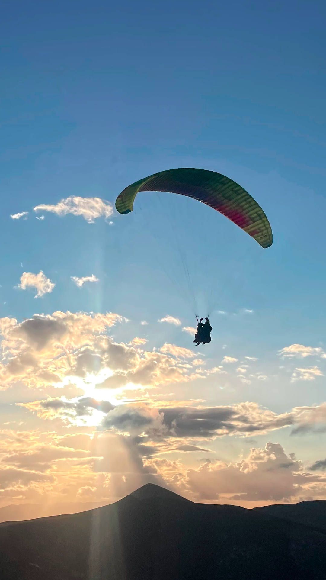 Ein Tandem-Gleitschirm fliegt im dynamischen Aufwind der untergehenden Sonne entgegen.