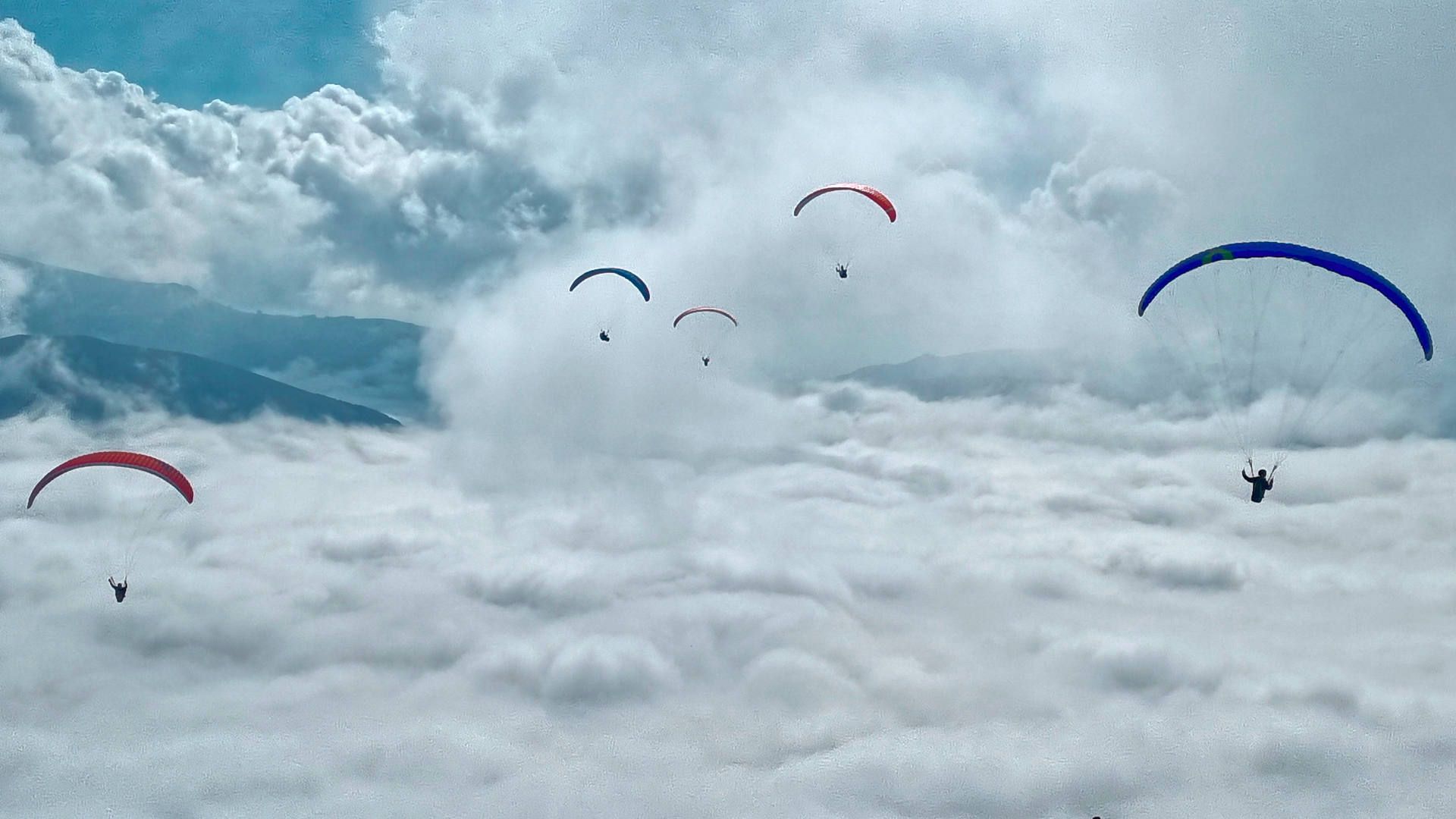 Fünf Gleitschirme fliegen über das sich in Auflösung begriffene Nebelmeer in der Ebene von Castelluccio hinaus.