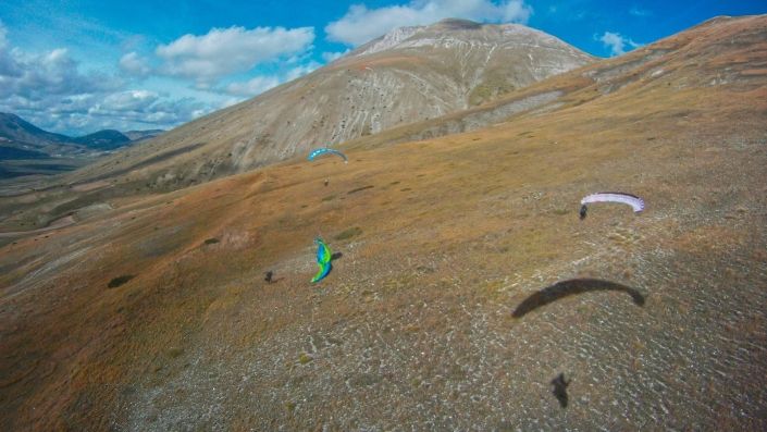 Luftaufnahme am Monte Vettore: Aus Pilotenperspektive sieht man einen anderen fliegenden Gleitschirm und am Boden zwei startbereite Piloten.