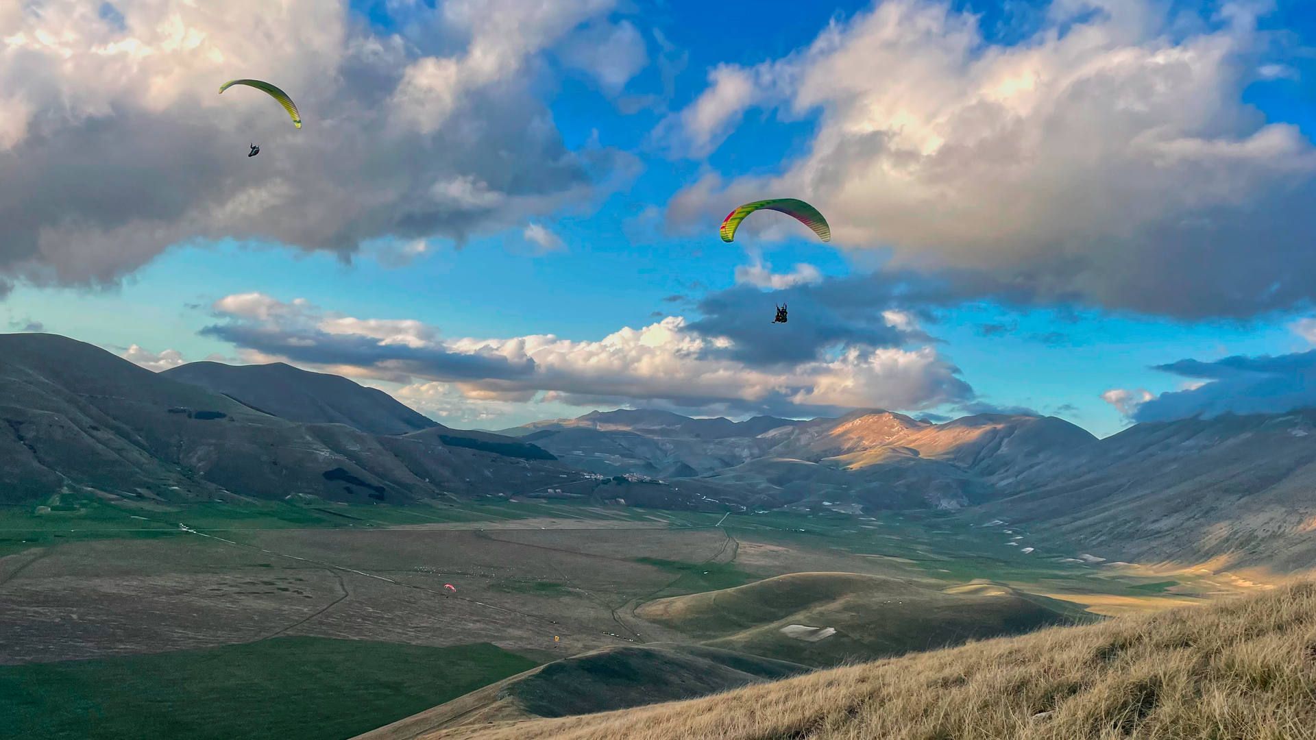 Ein Tandem- und ein Sologleitschirm kosten die letzten Aufwinde des Tages über der Ebene von Castelluccio aus.