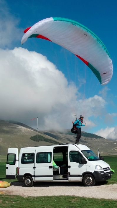 Ein Gleitschirmpilot steht mit seinem Miniwing auf dem Dach eines Personenbusses und kontrolliert den Schirm im laminaren Wind.