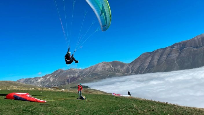 Ein Gleitschirmpilot plant eine Toplandung am Startplatz am Monte Veletta über dem Nebelmeer.