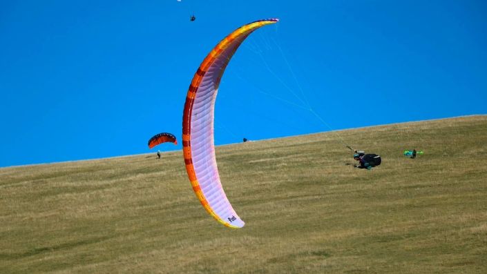 Hoch aufgeschaukelte Rollpendel eines Gleitschirmpiloten am Übungshang in der Ebene von Castelluccio.