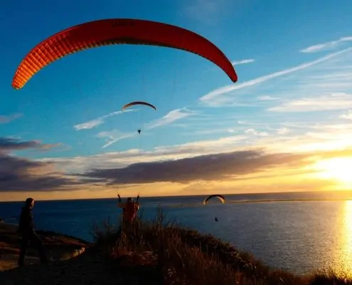 Abendliches Soaring für drei Gleitschirmpiloten an der Dune du Pyla kurz vor Sonnenuntergang.